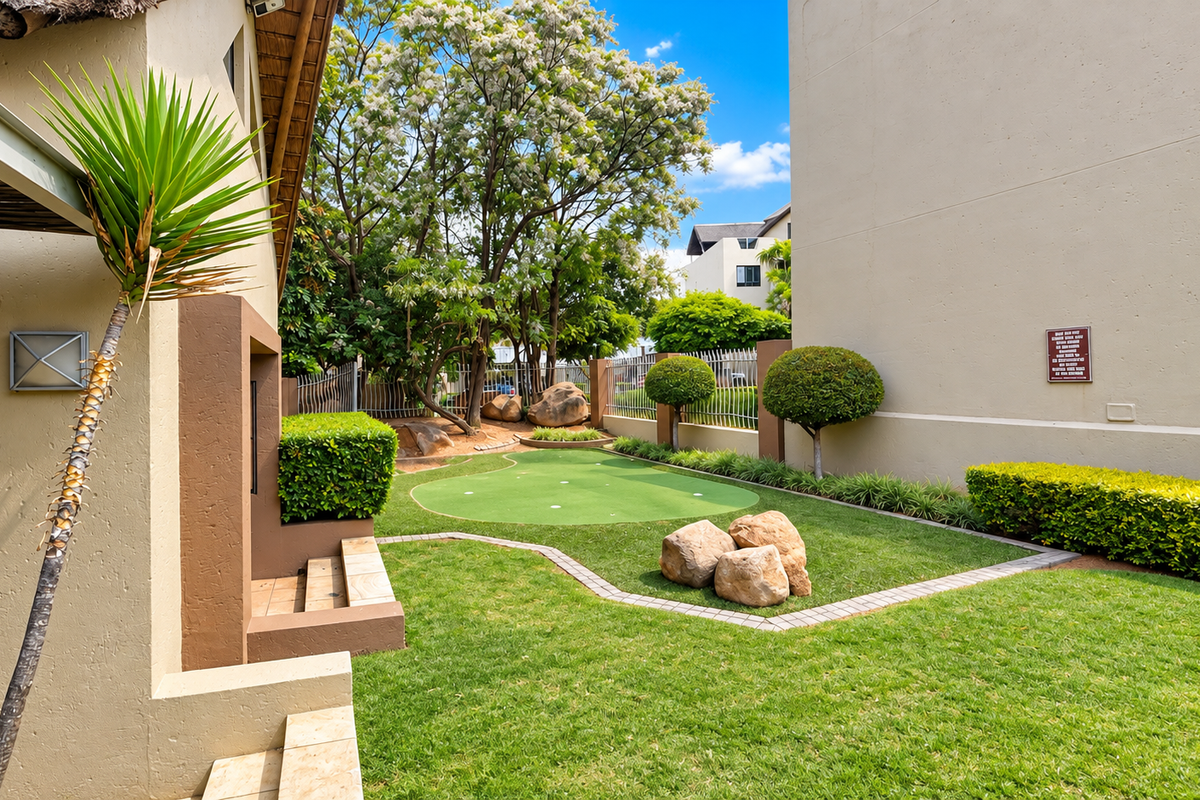 A well-maintained rear garden area featuring a private putting green, manicured lawn, and landscaped borders between apartment buildings.
