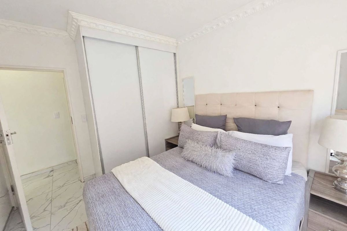 A well-maintained bedroom featuring built-in sliding door wardrobes, decorative ceiling cornicing, and modern marble-look floor tiles.