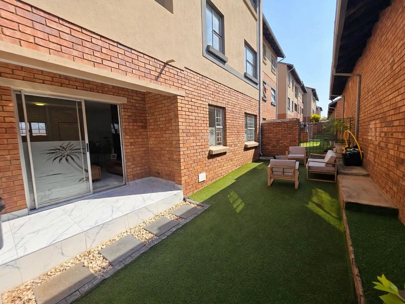 A well-maintained rear exterior featuring a tiled patio, artificial lawn, and brick facade with sliding door access to the interior living space.