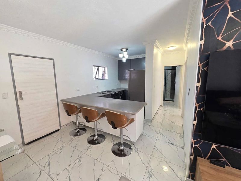 Modern open-plan kitchen featuring sleek cabinetry, a stainless steel breakfast bar, and elegant marble-look floor tiles, seamlessly connecting to the living area.