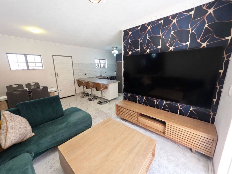 Open-plan living and kitchen area featuring marble-look floor tiles, a central kitchen island, and a modern feature wall with integrated television.