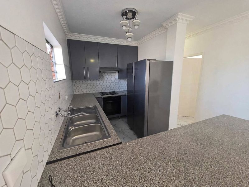 Modern kitchen featuring grey cabinetry, granite countertops, a hexagonal tile backsplash, and integrated appliances including a gas hob and oven.