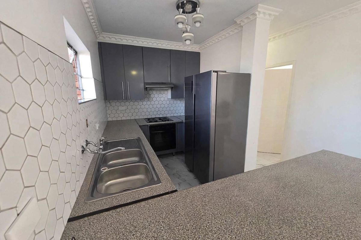 Modern kitchen featuring grey cabinetry, granite countertops, a hexagonal tile backsplash, and integrated appliances including a gas hob and oven.