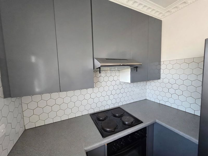 Modern kitchen featuring grey cabinetry, a sleek hexagon tile backsplash, integrated electric hob, oven, and extractor fan with decorative ceiling cornice detailing.