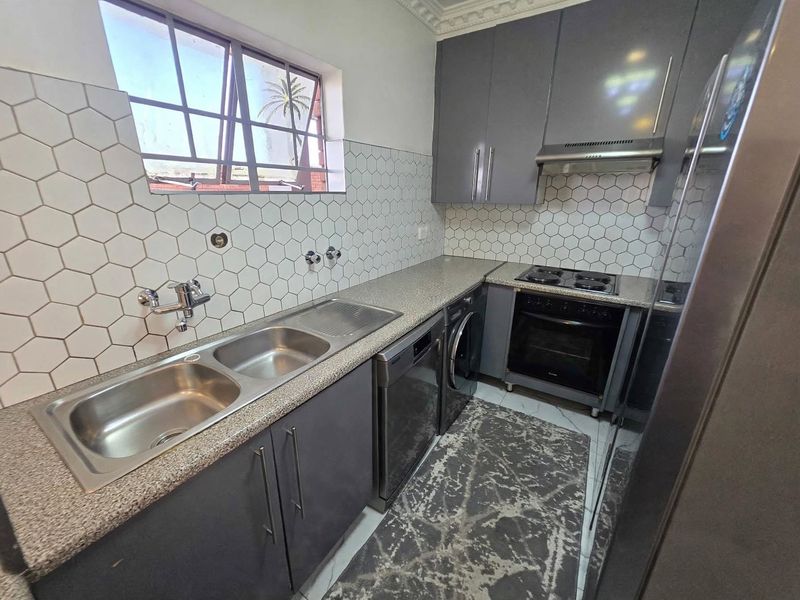Modern kitchen featuring grey cabinetry, hexagonal wall tiling, integrated oven and hob, and a double bowl stainless steel sink.