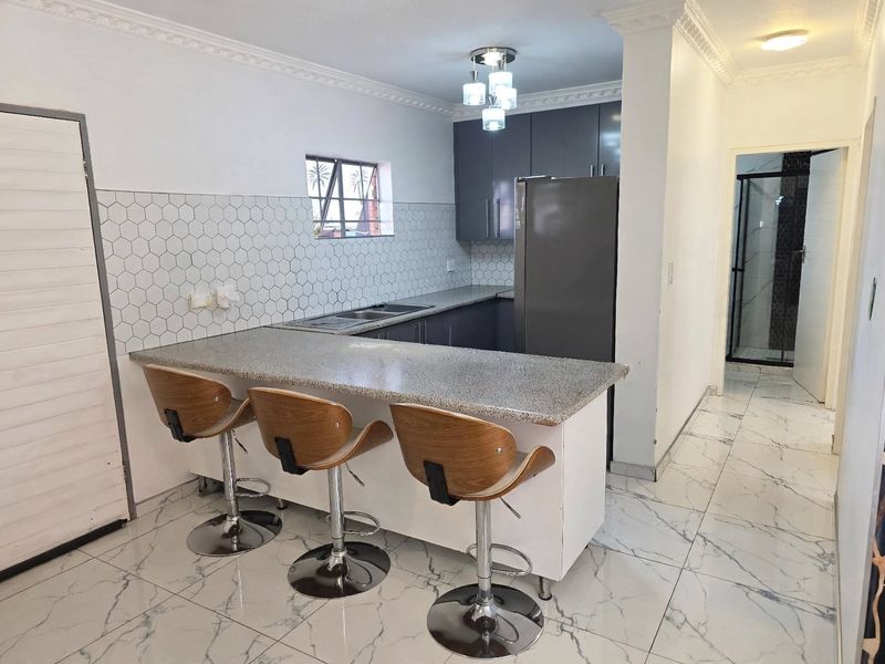 Modern kitchen featuring grey cabinetry, granite breakfast bar, hexagon tile backsplash, and marble-look floor tiles with elegant crown molding.