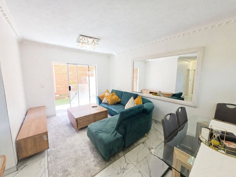 An open-plan living and dining area featuring marble-look floor tiles, crown molding, and a sliding glass door leading to an outdoor space.