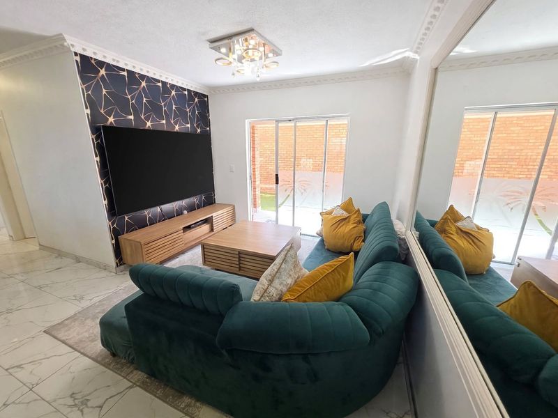 A well-maintained living room featuring a decorative feature wall, tiled flooring, ceiling cornice, and a sliding glass door providing access to the exterior.