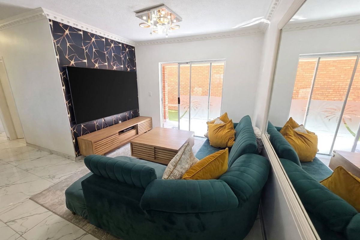 A well-maintained living room featuring a decorative feature wall, tiled flooring, ceiling cornice, and a sliding glass door providing access to the exterior.