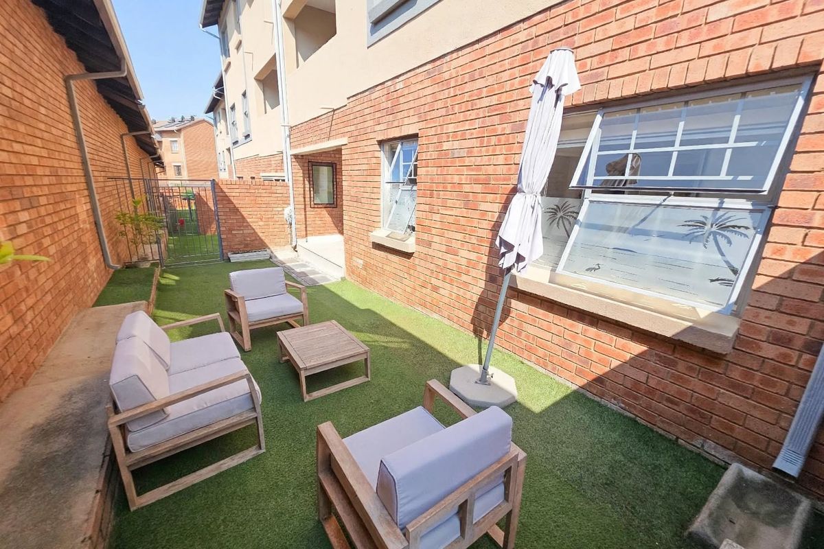 A private rear courtyard area featuring a brick facade, artificial lawn, and secure gated access, providing a low-maintenance outdoor space.