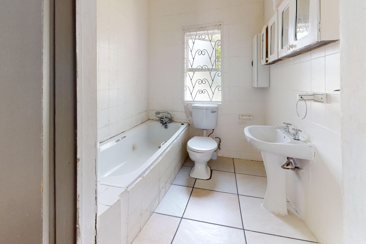 A dated bathroom featuring a bathtub, pedestal sink, and toilet, with white tiled walls and flooring, requiring cosmetic updates and modernization.