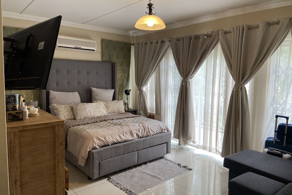 A well-maintained bedroom featuring tiled flooring, an air conditioning unit, and large sliding glass doors that provide ample natural light.