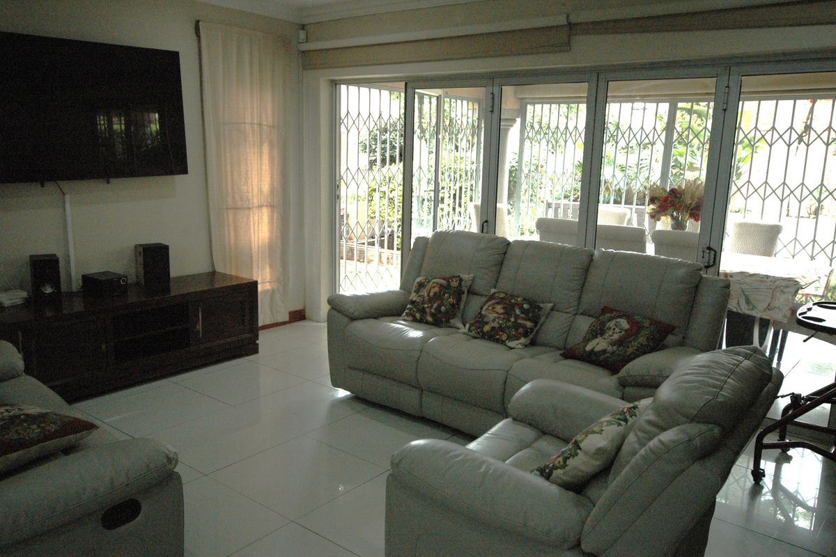 A bright living room featuring large sliding glass doors with security gates, providing direct access to the patio and natural light.