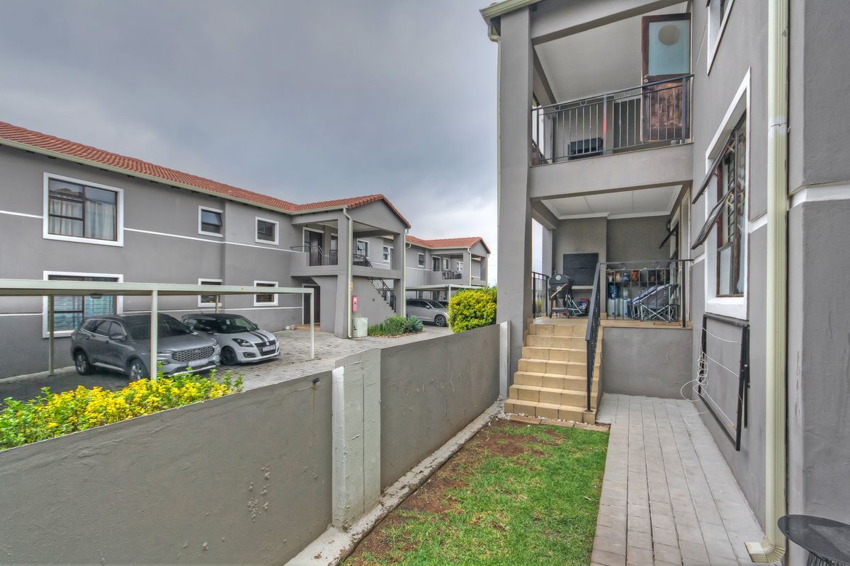 Exterior view of the apartment complex featuring a private terrace, tiled staircase, paved walkway, and communal parking area.