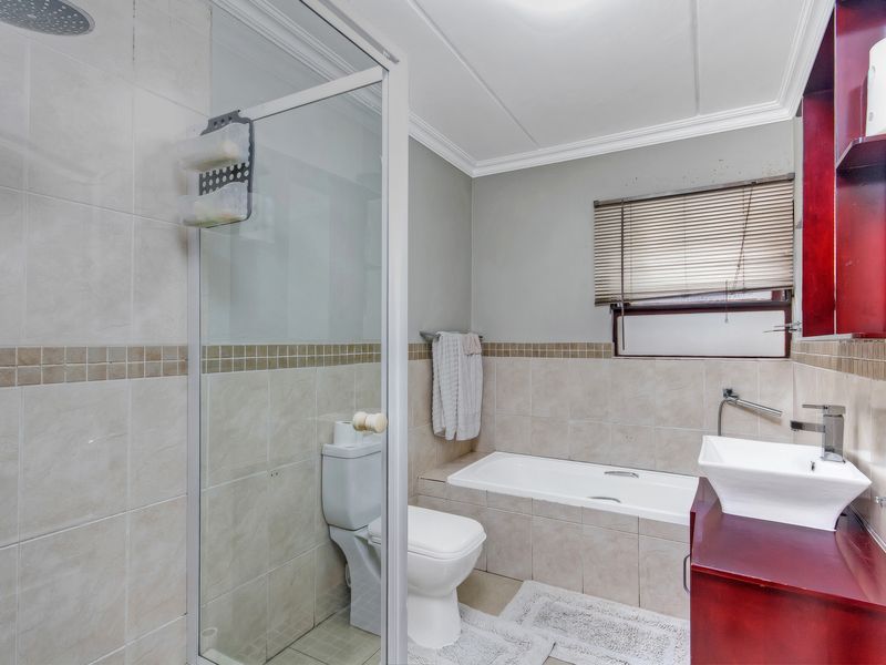 A functional bathroom featuring a glass-enclosed shower, a built-in bathtub, a vessel sink vanity, and neutral wall tiling.