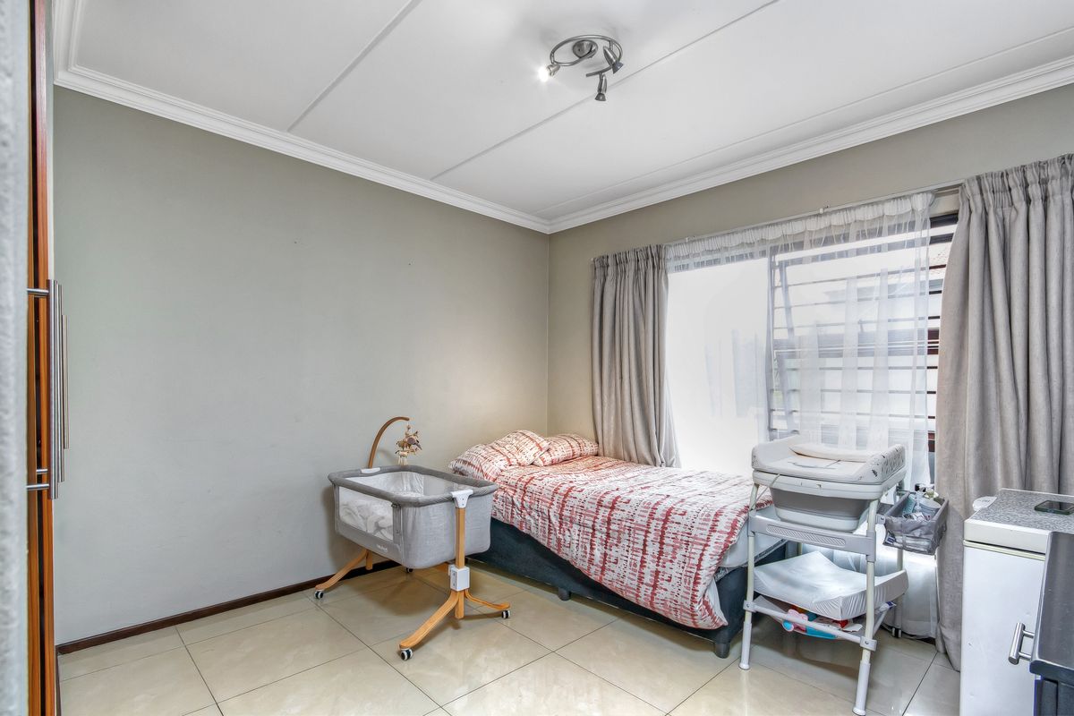 A functional bedroom featuring tiled flooring, built-in cupboard storage, and natural light through a large sliding window.