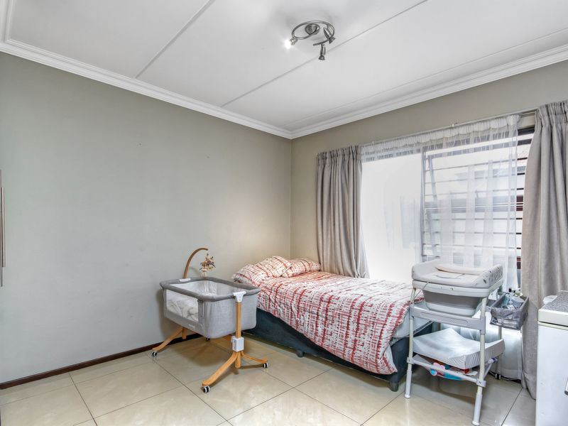 A functional bedroom featuring tiled flooring, built-in cupboard storage, and natural light through a large sliding window.