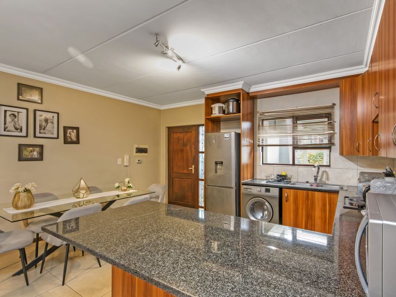 Open-plan kitchen and dining area featuring granite countertops, wooden cabinetry, and tiled flooring, creating a functional and connected living space.