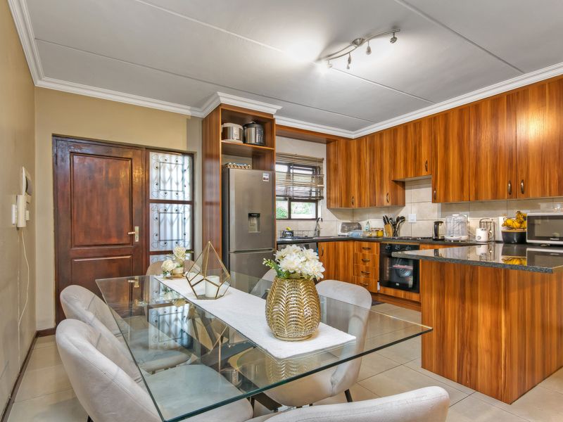 Open-plan kitchen and dining area featuring warm-toned wooden cabinetry, granite countertops, built-in oven, and tiled flooring with a functional layout.