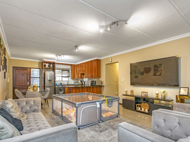 Open-plan living and kitchen area featuring tiled flooring, coved ceilings, and wood-finish kitchen cabinetry in a functional layout.