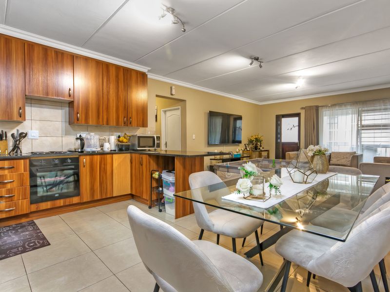 Open-plan living and dining area featuring a functional kitchen with wooden cabinetry, granite countertops, built-in oven, and tiled flooring throughout.