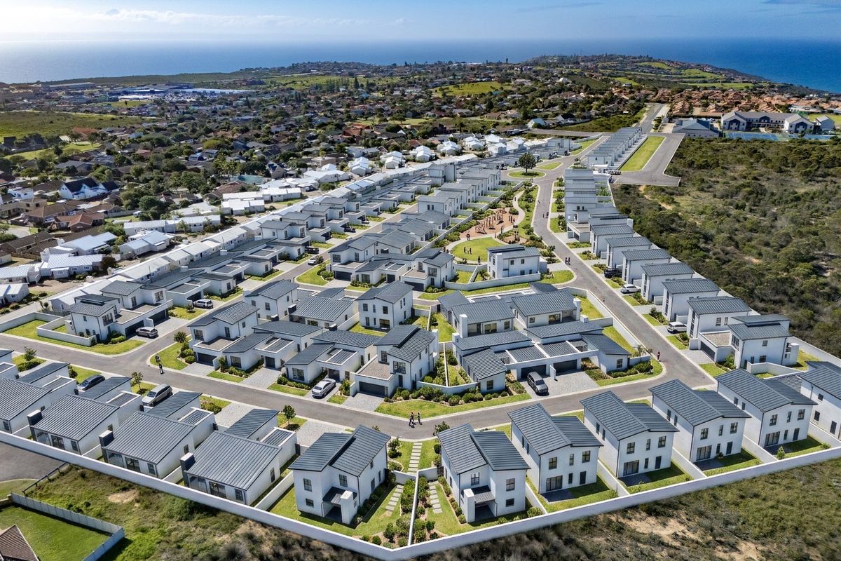 Aerial view of a modern residential estate featuring uniform housing units, paved streets, and landscaped communal areas with coastal views in the background.