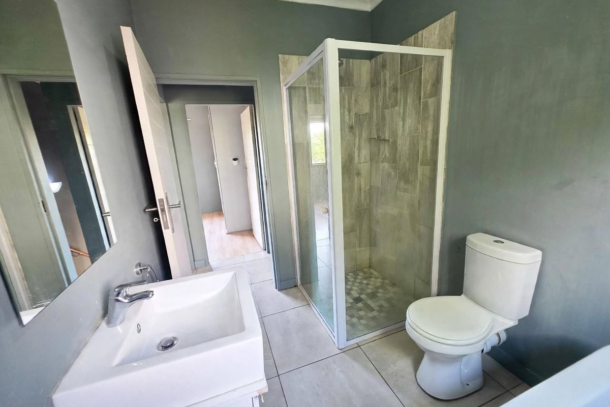 A modern, clean bathroom featuring a glass-enclosed shower, a white vanity basin, and a standard toilet with neutral grey wall finishes.