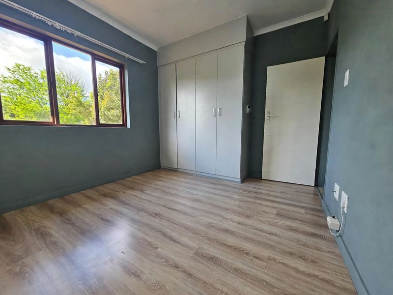 A bright, empty bedroom featuring modern laminate flooring, dark grey walls, and built-in cupboards, offering a clean and neutral space ready for personalization.