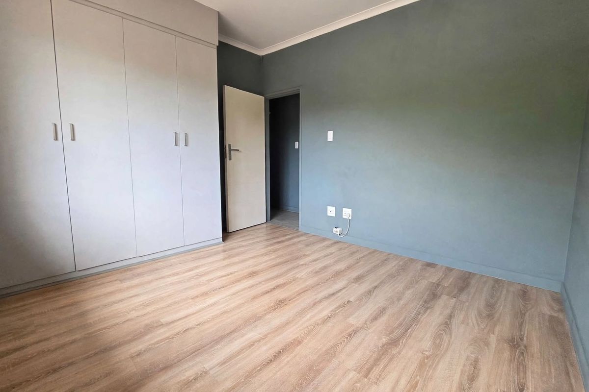 A clean, empty bedroom featuring modern laminate flooring, built-in cupboards, and a neutral grey accent wall, ready for personalization.