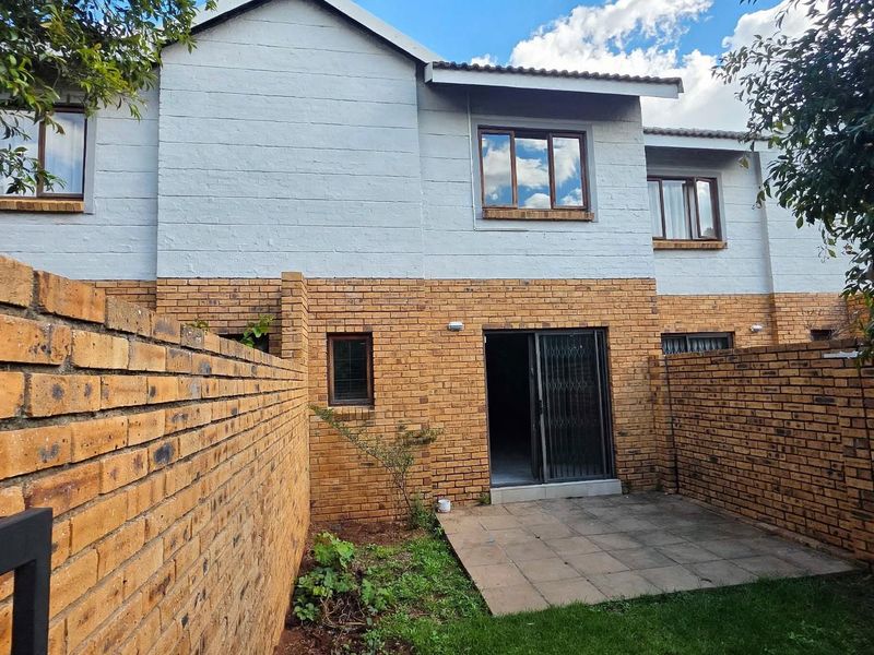 Rear view of a townhouse featuring a private paved patio, brick boundary walls, and a sliding door entrance with security gate.