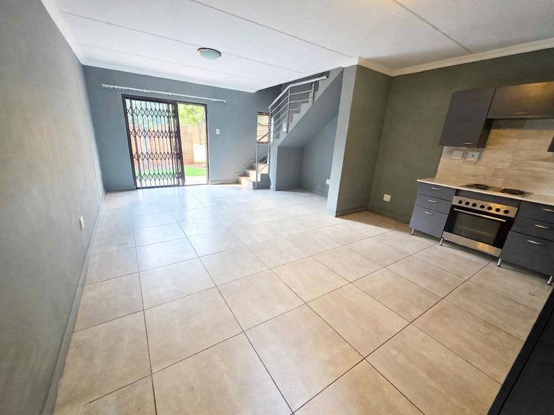 Open-plan living area featuring tiled floors, a modern kitchen with built-in appliances, and a staircase leading to the upper level with access to the garden.