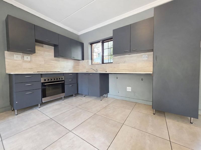 Modern kitchen featuring dark grey cabinetry, tiled splashbacks, built-in oven and hob, and tiled flooring. The space is ready for final appliance installation.