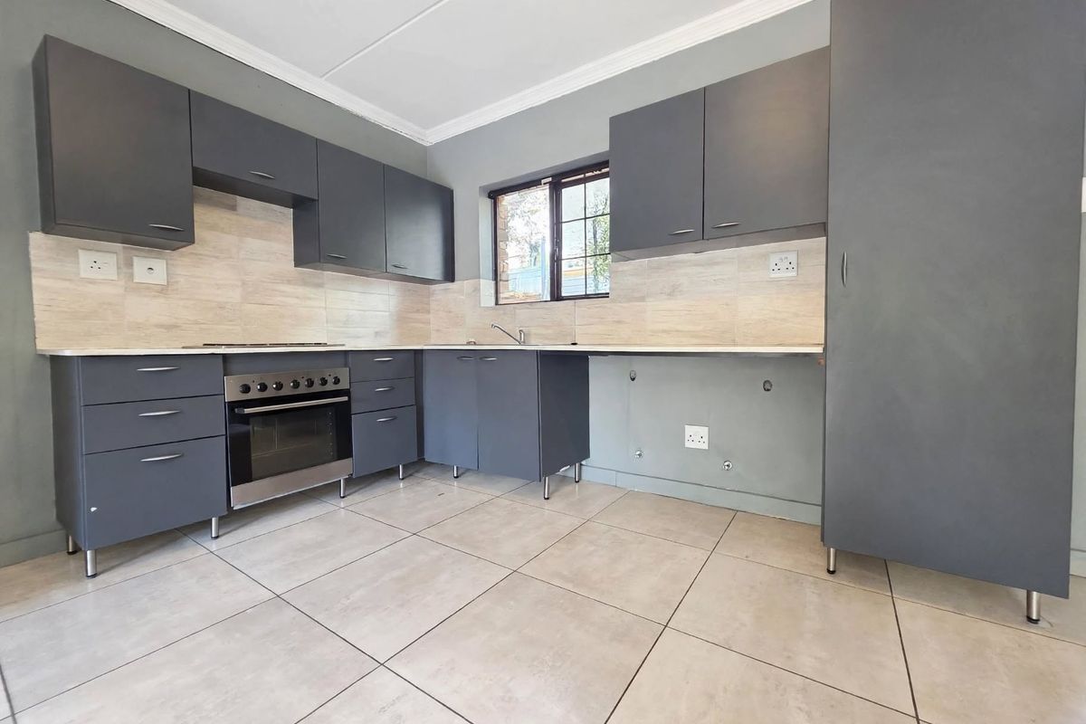 Modern kitchen featuring dark grey cabinetry, tiled splashbacks, built-in oven and hob, and tiled flooring. The space is ready for final appliance installation.