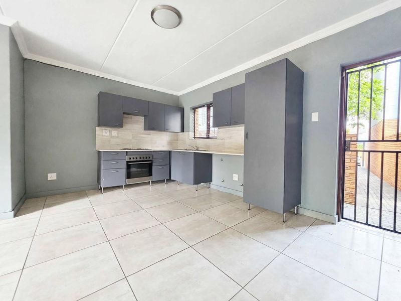 A clean, modern kitchen featuring grey cabinetry, built-in oven and hob, tiled flooring, and direct access to the exterior via a security gate.