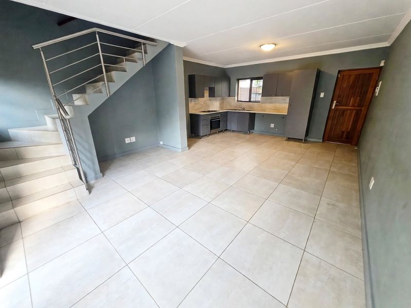 Spacious open-plan living area featuring tiled floors, a modern staircase with stainless steel balustrade, and a functional kitchen with built-in cabinetry and appliances.