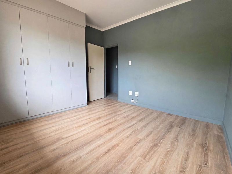 A clean, empty bedroom featuring modern laminate flooring, built-in cupboards, and a neutral grey accent wall, ready for personalization.