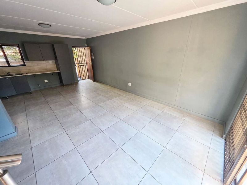 An open-plan living and kitchen area featuring neutral grey walls, large format floor tiles, and compact built-in kitchen cabinetry.