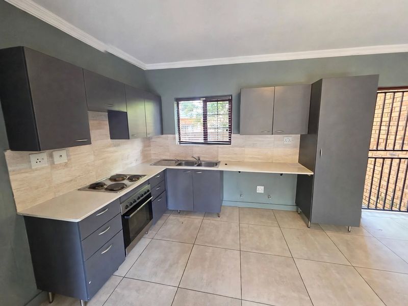 Modern kitchen featuring dark grey cabinetry, light tiled flooring, built-in oven and hob, and a double sink with a window view.