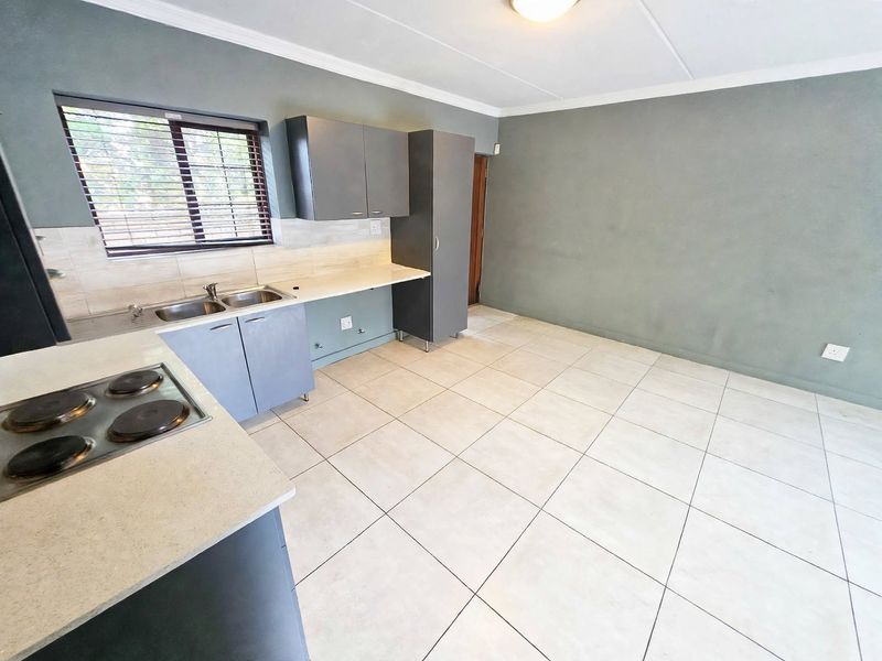A clean, empty kitchen featuring grey built-in cabinetry, a double basin sink, an electric hob, and neutral tiled flooring.