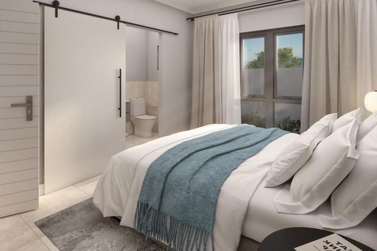 Modern bedroom featuring a sliding barn door leading to an en-suite bathroom, neutral finishes, and large windows allowing for natural light.