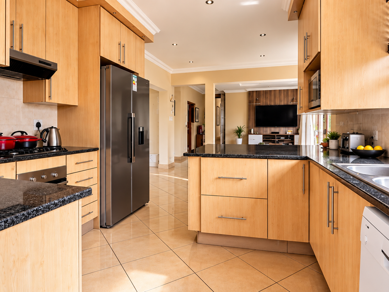 Modern open-plan kitchen featuring light-wood cabinetry, granite countertops, and integrated stainless steel appliances, flowing seamlessly into the adjacent living area.