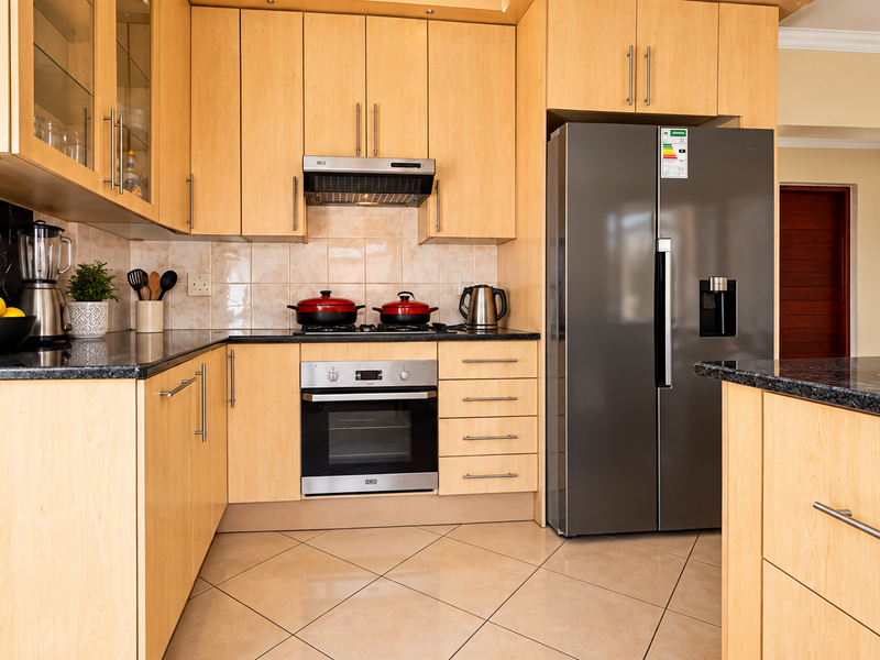 A well-maintained kitchen featuring light wood cabinetry, granite countertops, built-in oven, hob, and extractor fan, complemented by tiled flooring and backsplash.