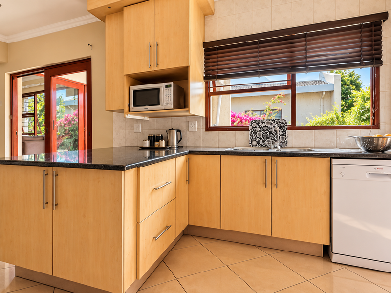 A well-maintained kitchen featuring light wood cabinetry, granite countertops, built-in microwave, and integrated dishwasher, with natural light flowing from the adjacent living area.