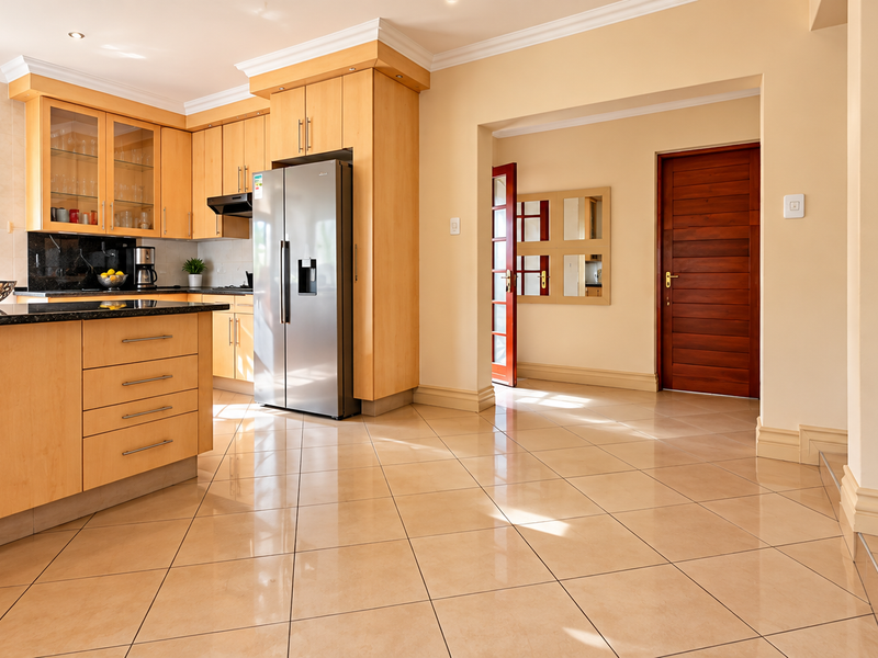 A well-maintained kitchen featuring light wood cabinetry, granite countertops, and polished tile flooring, leading into a hallway with a solid wood door.