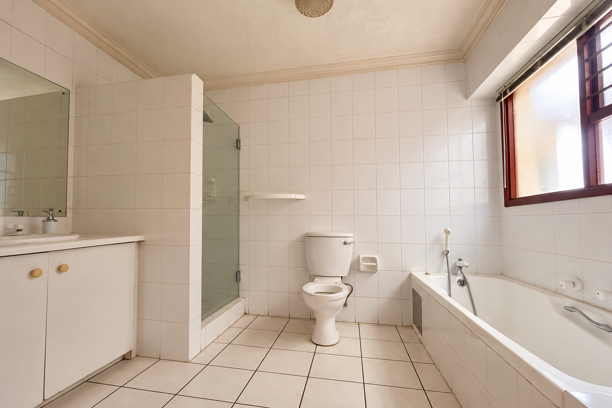 A functional bathroom featuring a vanity cabinet, glass shower enclosure, toilet, and bathtub with white tiled walls and flooring.