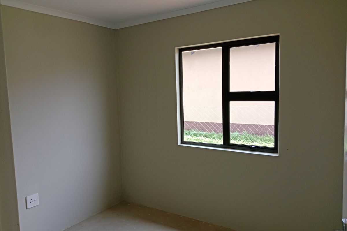 A clean, empty bedroom featuring neutral walls, an aluminium-framed window, and a standard electrical outlet, ready for personalization.