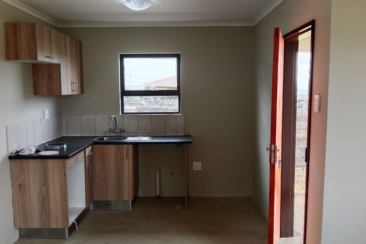 A compact, empty kitchen featuring wood-look laminate cabinetry, a stainless steel sink, and tiled splashback, ready for appliance installation.