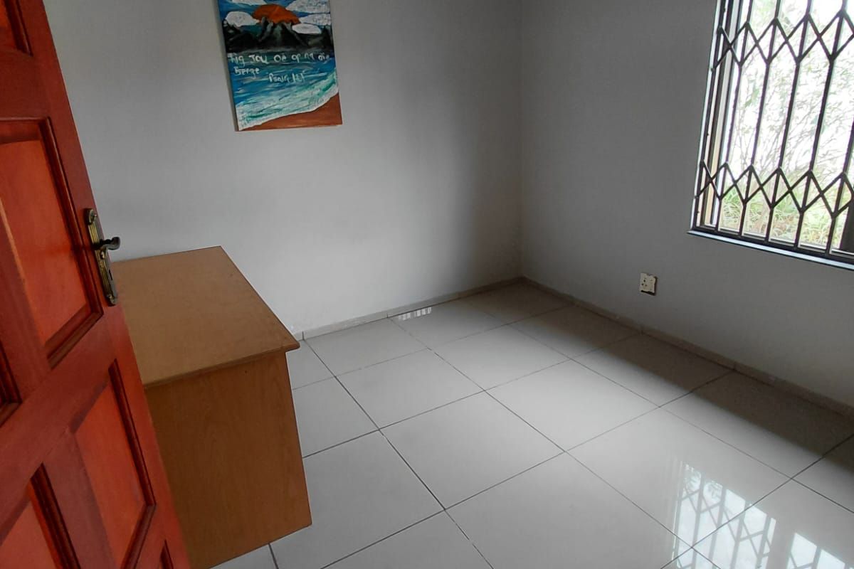 A clean, empty bedroom featuring neutral tiled flooring, a security gate on the window, and a simple pendant light fixture.