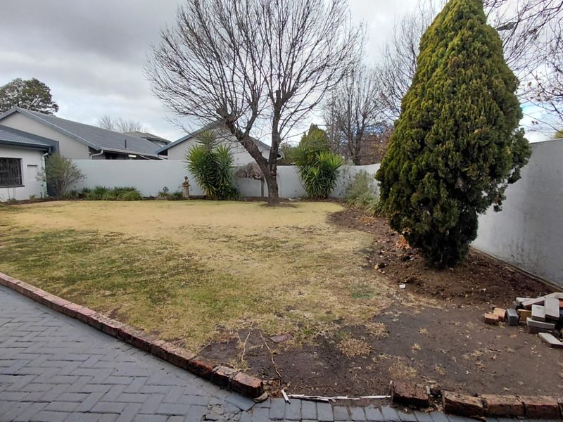 A rear garden featuring a paved patio area, brick edging, and a lawn enclosed by boundary walls.
