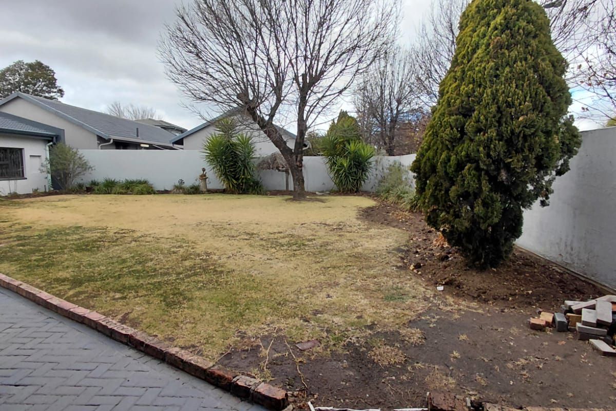 A rear garden featuring a paved patio area, brick edging, and a lawn enclosed by boundary walls.